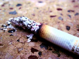 A burning out, ashy cigarette sitting on a pavement.
