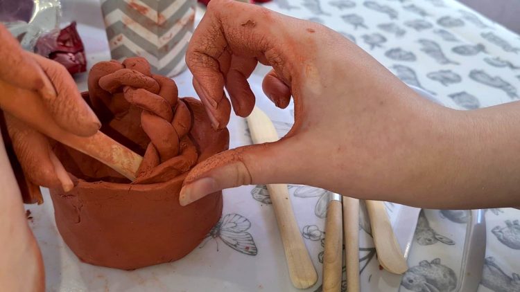 A person making a terracotta pottery basket with plaited handle.
